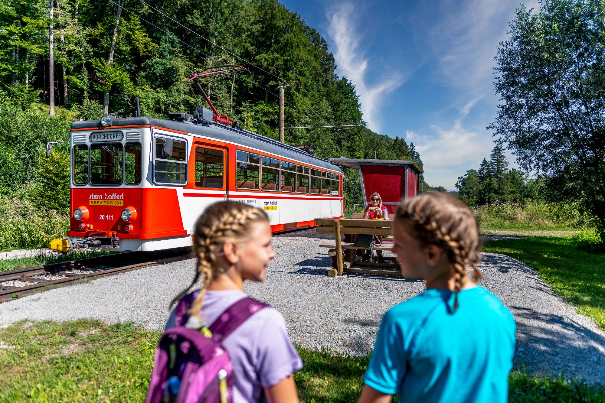 Zwei Mädels stehen vor der Vorchdorferbahn ihre Mutter sitzt auf einer Bank